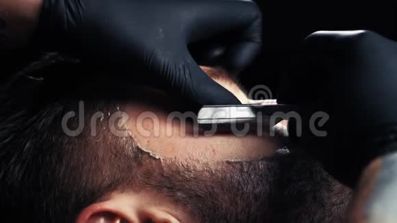 一个英俊的男人用剃刀在一家理发店的专业理发师那里刮胡子视频的预览图