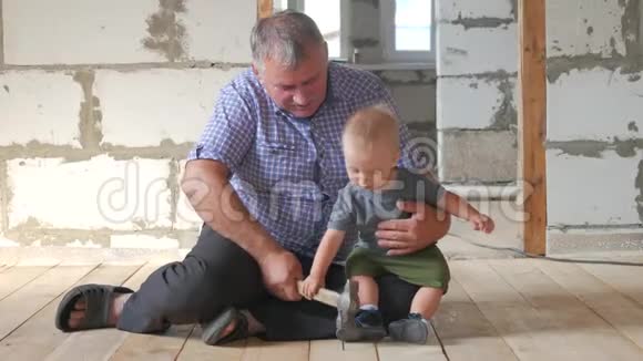 在工地上工作的爷爷和孙子祖父教他的孙子锤钉子视频的预览图
