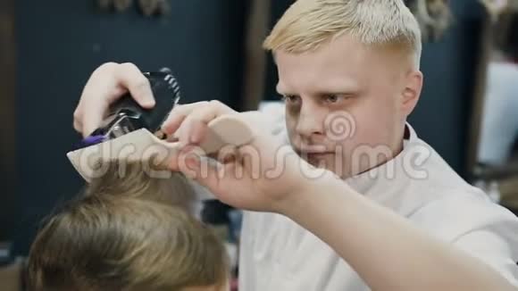 专业的金发美发师在梳子和电动剃须刀的帮助下在湿发上做了一个新的发型男理发师视频的预览图