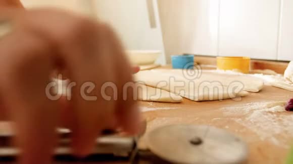 特写4k镜头女性手拿圆刀刀切面团在木制厨房台面上视频的预览图