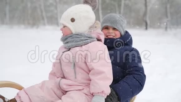 穿着粉红色连衣裙的男孩和小女孩在下雪的冬天滑雪父母在下雪时带着儿子和女儿拉雪橇视频的预览图
