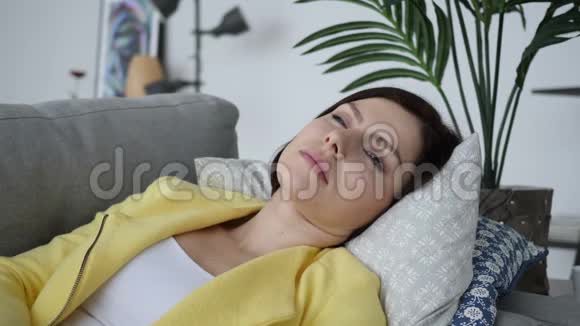 头痛紧张的女人躺在家里的沙发上视频的预览图