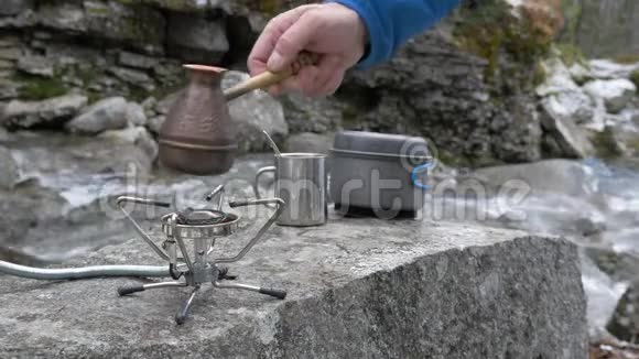 在徒步旅行中咖啡是在便携式燃气燃烧器上准备的特写镜头在一条山河的岸边视频的预览图