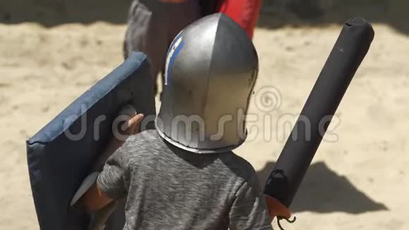 穿着塑料盔甲的男孩在竞技场上训练用棍子击剑孩子们游戏慢动作视频的预览图