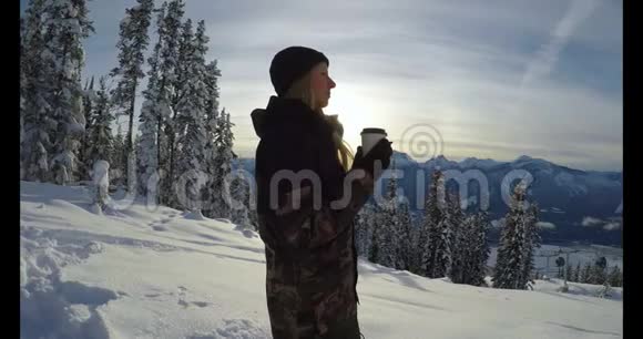 带着咖啡杯的女人站在白雪覆盖的风景上视频的预览图