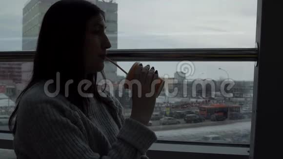 年轻女子在咖啡馆里喝着刚榨的果汁看着窗外的特大城市背景视频的预览图