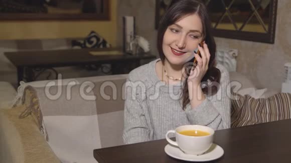 在咖啡馆里喝茶和打电话的年轻女子视频的预览图