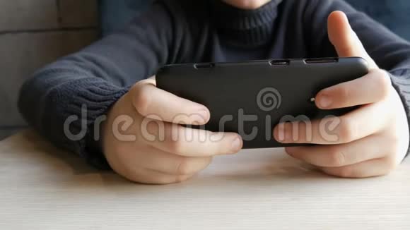 少年男孩的手在一家时尚的咖啡馆里玩黑色智能手机相机在运动视频的预览图