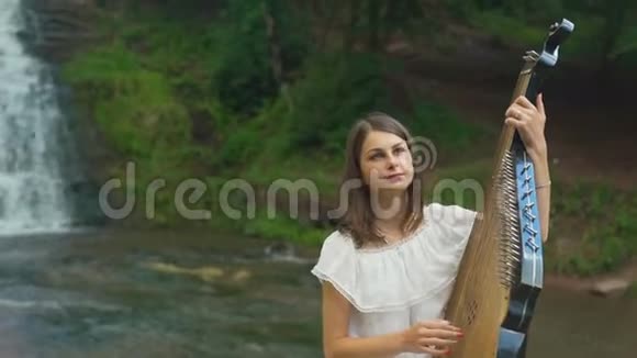 女性的手轻轻地触到瀑布处的琴弦视频的预览图