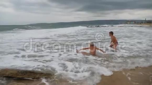 宝贝在海滩上在海浪中两个男孩在金沙上玩冲浪视频的预览图