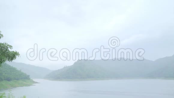 年轻的亚洲甜蜜的一对夫妇感到快乐用浪漫的时间打雨穿着雨衣站在湖边视频的预览图