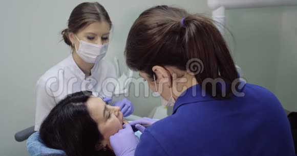 牙医为一位年轻女性做检查和牙科清洁护士坐在旁边帮助病人快乐微笑视频的预览图