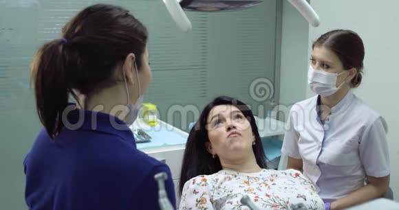 牙医用镜子检查一位年轻女子的牙齿牙科护士坐在旁边帮忙病人高兴地打开视频的预览图