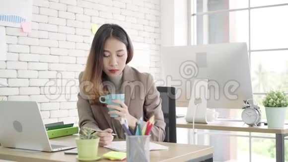 两位年轻的亚洲女商人在小企业的办公室里一起工作坐着看报告或文件视频的预览图