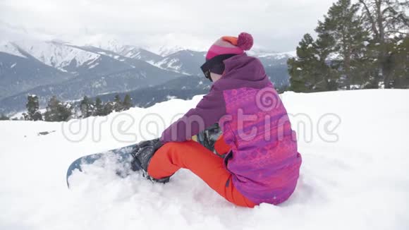 坐在山顶上享受山景的滑雪板女孩雪山上的运动女人美丽动人视频的预览图