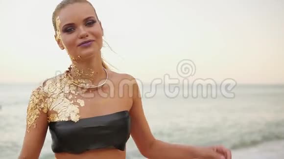 年轻迷人的漂亮模特穿着泳衣在海滩上摆姿势穿着金色皮肤黑色泳衣的女孩视频的预览图