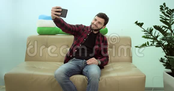 幸福微笑的男人拿着手机坐在沙发上自拍视频的预览图