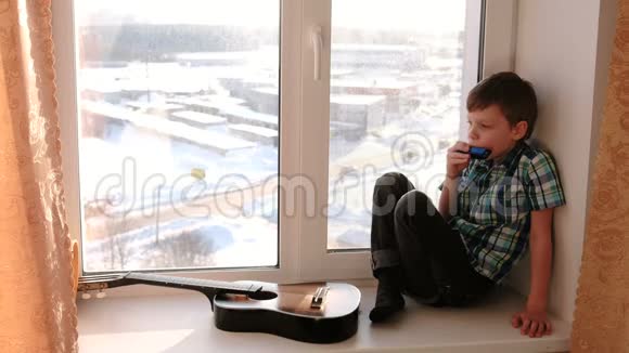 演奏乐器男孩坐在窗台上玩口风琴视频的预览图