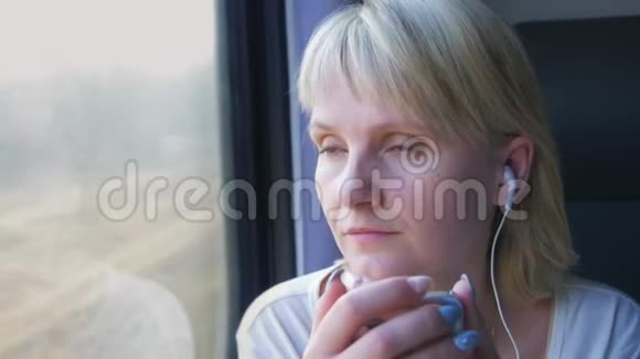 年轻的高加索女人坐在火车车厢里手里拿着智能手机听耳机音乐视频的预览图