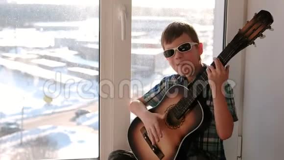 演奏乐器戴太阳镜的男孩会弹吉他坐在窗台上唱歌视频的预览图