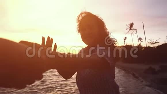 开朗的年轻女人牵着她朋友的手在美丽的夕阳下示意他沿着海滩散步跟我来视频的预览图
