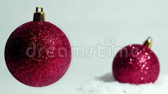 圣诞节装饰两个红球一个在雪地上另一个在白色背景上摆动视频的预览图