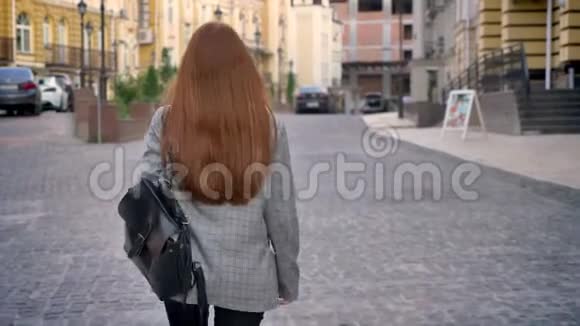 年轻的女人留着长长的姜发在城市里散步回头看拿着背包城市街道背景回来视频的预览图