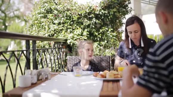 一家人在户外咖啡馆吃早餐可爱的女孩和妈妈在露台上喝新鲜果汁和吃牛角面包视频的预览图