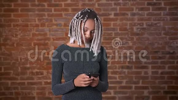 年轻的非洲女孩用智能手机打字背景中的砖墙视频的预览图