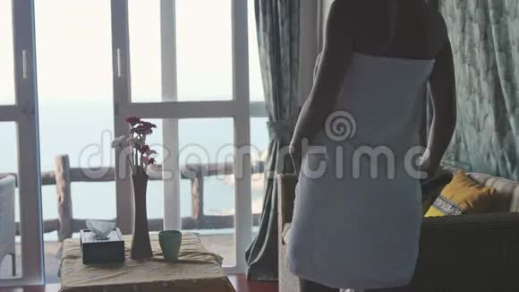 年轻女子裹着毛巾在平房里看电视旅行时在热带岛屿上喝咖啡海景视频的预览图