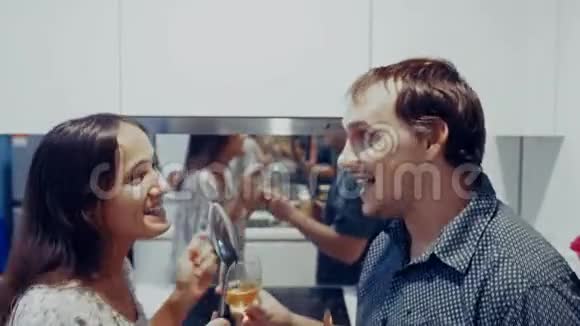 有魅力的年轻快乐的一对夫妇在家厨房做饭时用瓢泼酒跳舞唱歌视频的预览图