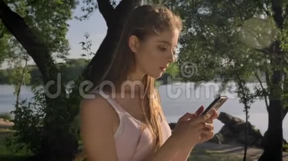 在河边公园年轻漂亮的女人在手机上发短信微笑着美丽的景色视频的预览图