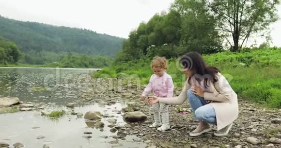 母亲和女儿把石头扔进河里母亲的快乐时刻给五个山脉背景视频的预览图
