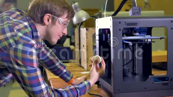 一个快乐的工程师拿着一个白色的原型头看着一个工作的3d打印机4K视频的预览图