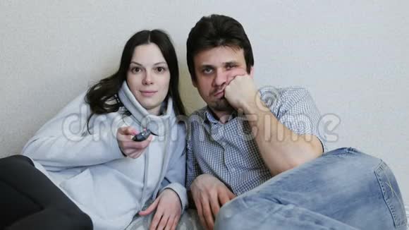 两个人躺在沙发上看电视女人有兴趣地切换频道和观看男人很无聊视频的预览图