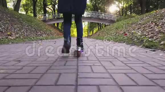 在秋天公园的人行道上小女孩的腿骑着滑板车斯坦迪卡姆视频的预览图