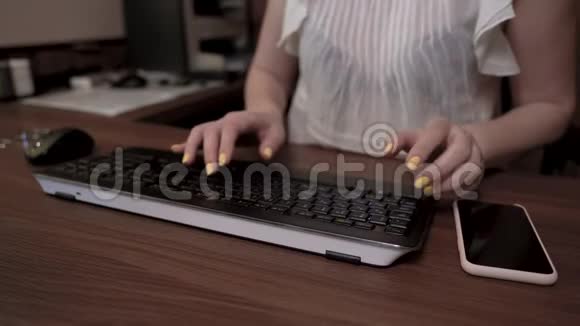 女人的手拿着黄色的指甲在键盘上打字手机在木桌上视频的预览图