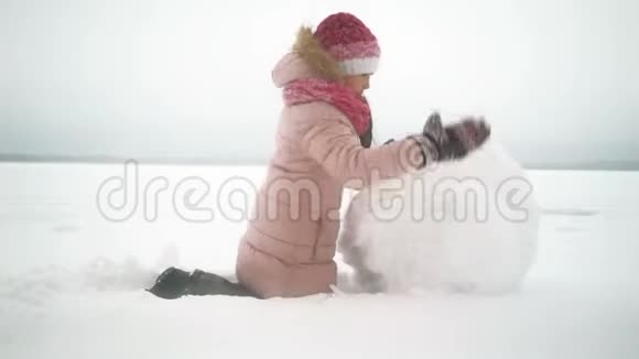 女孩在冬天为雪人滚动大雪球视频的预览图