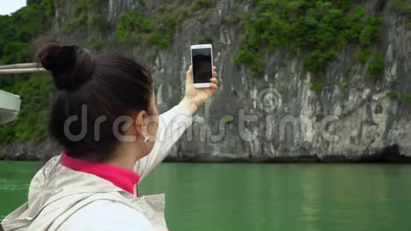 穿米色夹克的黑发女人在海湾里拍照乘船旅行一个美丽的绿色海湾步行视频的预览图