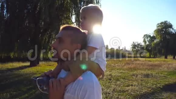 幸福的家庭走在草地上爸爸指着他的孩子坐在他肩膀上的小男孩视频的预览图