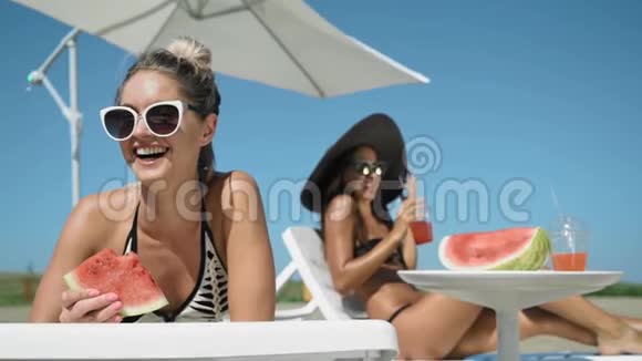 女孩们在沙滩上笑着吃着西瓜躺在躺椅上视频的预览图