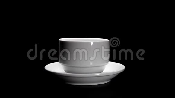 白色的杯子和咖啡的盘子在黑色的背景上旋转视频的预览图