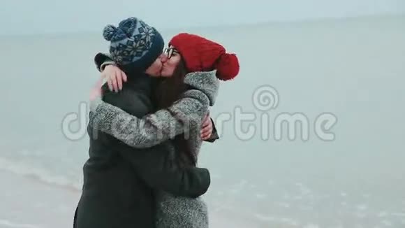 年轻夫妇穿着灰色的冬衣亲吻着灰色的天空和大海视频的预览图