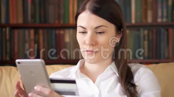 穿着白色衬衫的女商人坐在客厅的沙发上用手机上网购买信用卡视频的预览图