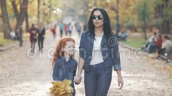 一位美丽的母亲和她可爱的小女儿在秋天的公园里散步他们在人群中间走来走去视频的预览图