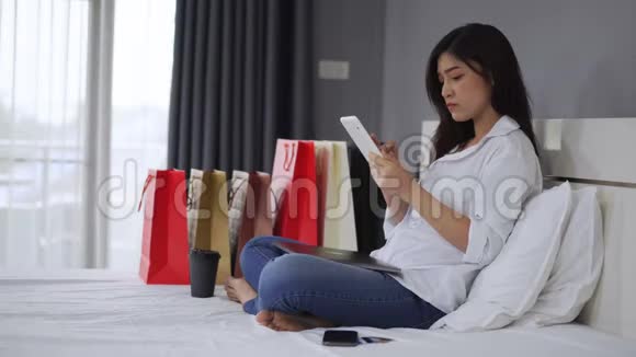 使用平板电脑的衣着讲究的女性在卧室里有网购的问题视频的预览图