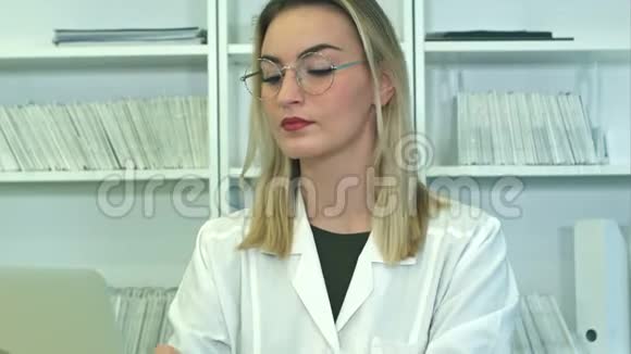 戴眼镜的漂亮女医生用笔记本电脑坐在前台视频的预览图
