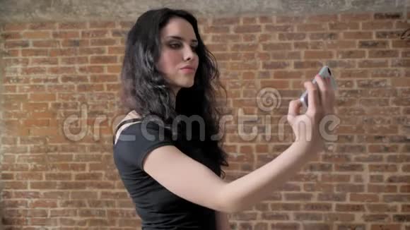 年轻迷人的黑发女孩正在智能手机上自拍沟通观念砖背景视频的预览图