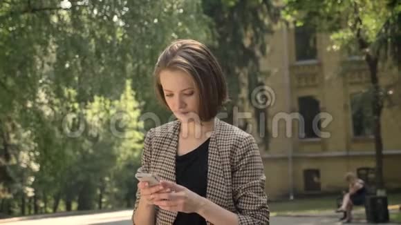 年轻可爱的女孩白天在公园的智能手机上输入信息夏天在公园里交流理念视频的预览图