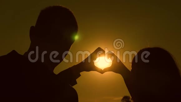 太阳在手里一个女孩和她的男朋友在美丽的日落对面用手做心形视频的预览图